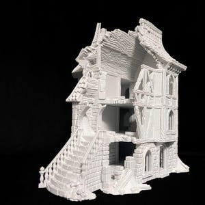 Puede incluir: Una maqueta en miniatura blanca y sin pintar de un edificio en ruinas de varias plantas, con ladrillos a la vista, entramado de madera, un tejado dañado con texturas de veta de madera y una escalera exterior que conduce al segundo nivel.