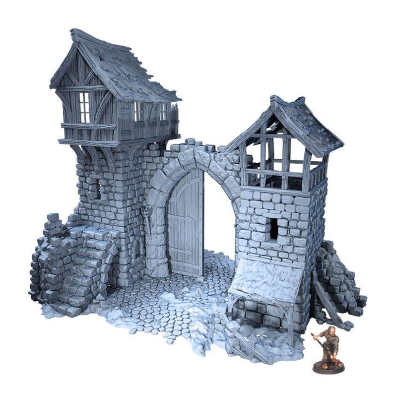Puede incluir: Una maqueta gris de una puerta de castillo con una puerta de madera, muros de piedra y dos torres de vigilancia. Las torres tienen tejados de madera y peque&ntilde;as ventanas. Una peque&ntilde;a figura de una persona est&aacute; de pie cerca de la puerta.