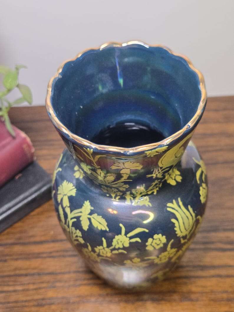 May include: A dark blue vase with a scalloped rim and gold trim. The vase features a floral pattern in a lighter shade of yellow. The vase is a decorative item.