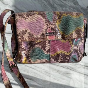 May include: Aimee Kestenberg crossbody bag with a snakeskin pattern in shades of pink, green, yellow, and brown. The bag has a long, adjustable strap and a flap closure. The brand name "AIMEE" is visible on the front.