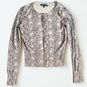 Peut inclure: Cardigan à boutons avec un motif peau de serpent dans les tons marron et crème. Ce pull à manches longues a un ourlet et des poignets côtelés, ainsi qu'un col rond. Le tissu tricoté est doux.