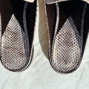 May include: Close-up of two brown and white snake-skin patterned loafers. The interior of the shoes features a similar pattern. The shoes are set against a light-colored surface.