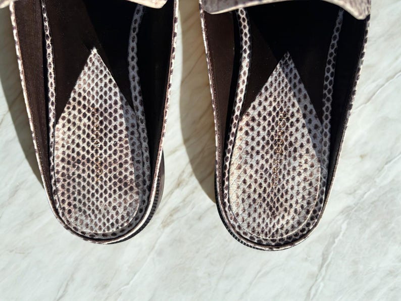 May include: Close-up of two brown and white snake-skin patterned loafers. The interior of the shoes features a similar pattern. The shoes are set against a light-colored surface.