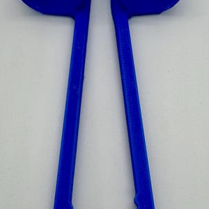 May include: A bright blue, 3D-printed tool with a unique shape. It features two long, parallel handles connected at the top by a curved bridge. The handles have a textured, scalloped edge near the bottom, and curved ends.