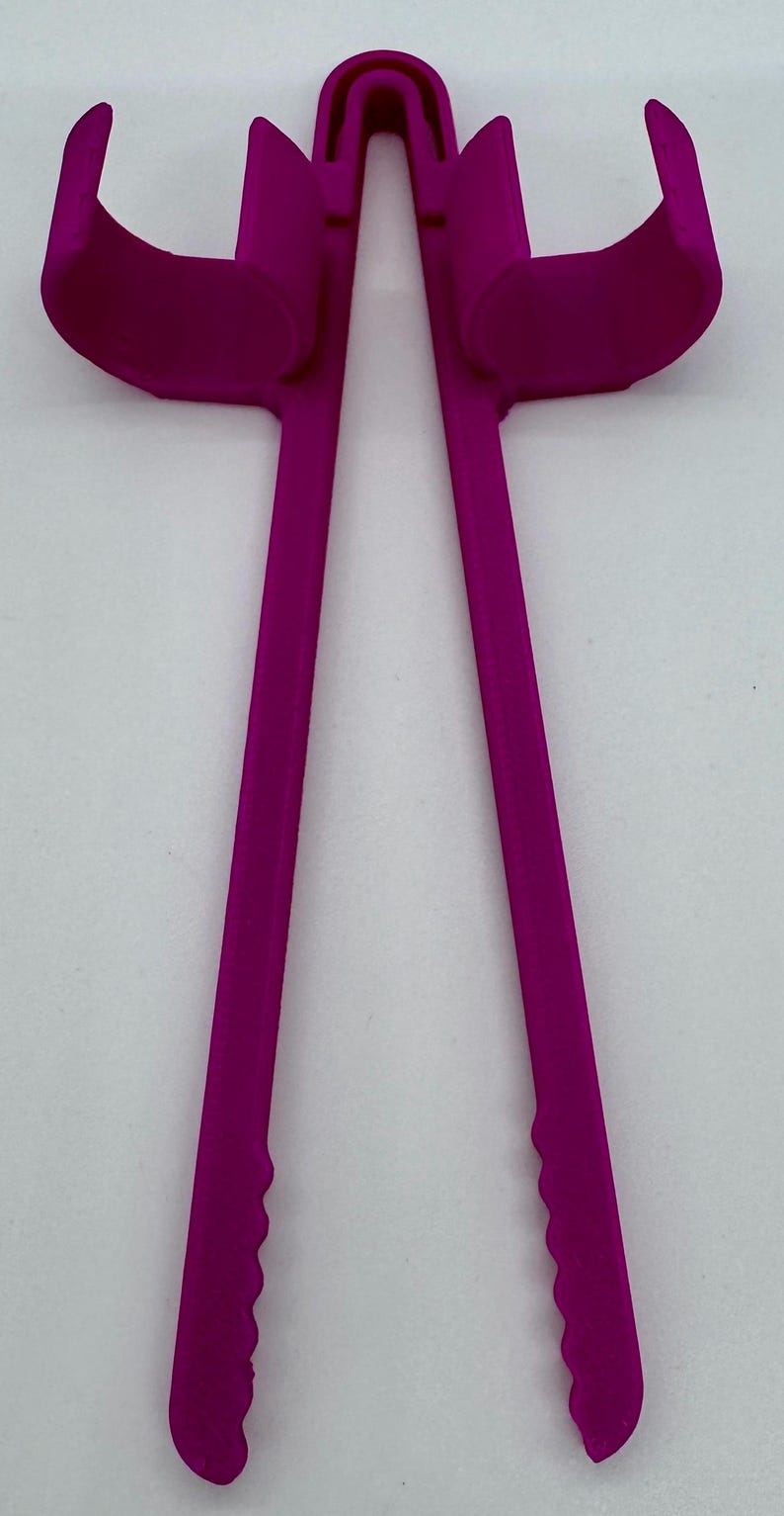 May include: A magenta-colored, plastic tool with a unique design. It features two curved arms connected by a bridge, with long, straight handles ending in a scalloped edge. The object is set against a plain white background.
