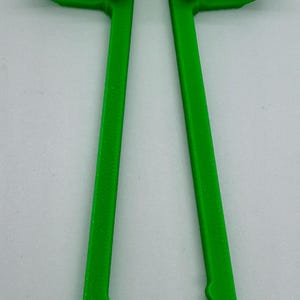 May include: Bright green 3D-printed tool with two curved arms and two long, parallel handles. The handles have a textured, scalloped edge. The tool is designed to hold or grip something.