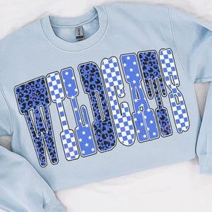 May include: A light blue sweatshirt with the word "WILDCATS" in large, bold letters across the front. The letters have a mix of patterns, including leopard print, checkered, and star designs. The sweatshirt has long sleeves and a crew neck.