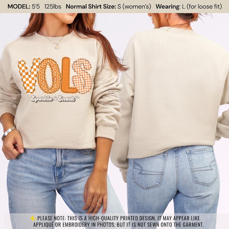 May include: Beige sweatshirt with the word "VOLS" in orange, with a checkerboard and dotted pattern. The text "Sparkle & Snark" is below the word "VOLS". The model is wearing a size L for a loose fit.