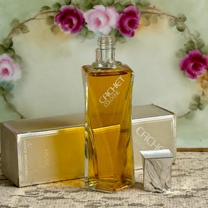 May include: A vintage Cachet Cologne bottle with a silver cap and a gold-colored liquid. The bottle is rectangular with a twisted design. The box is gold with the words "Prince Matchabelli" and "4 fl oz".