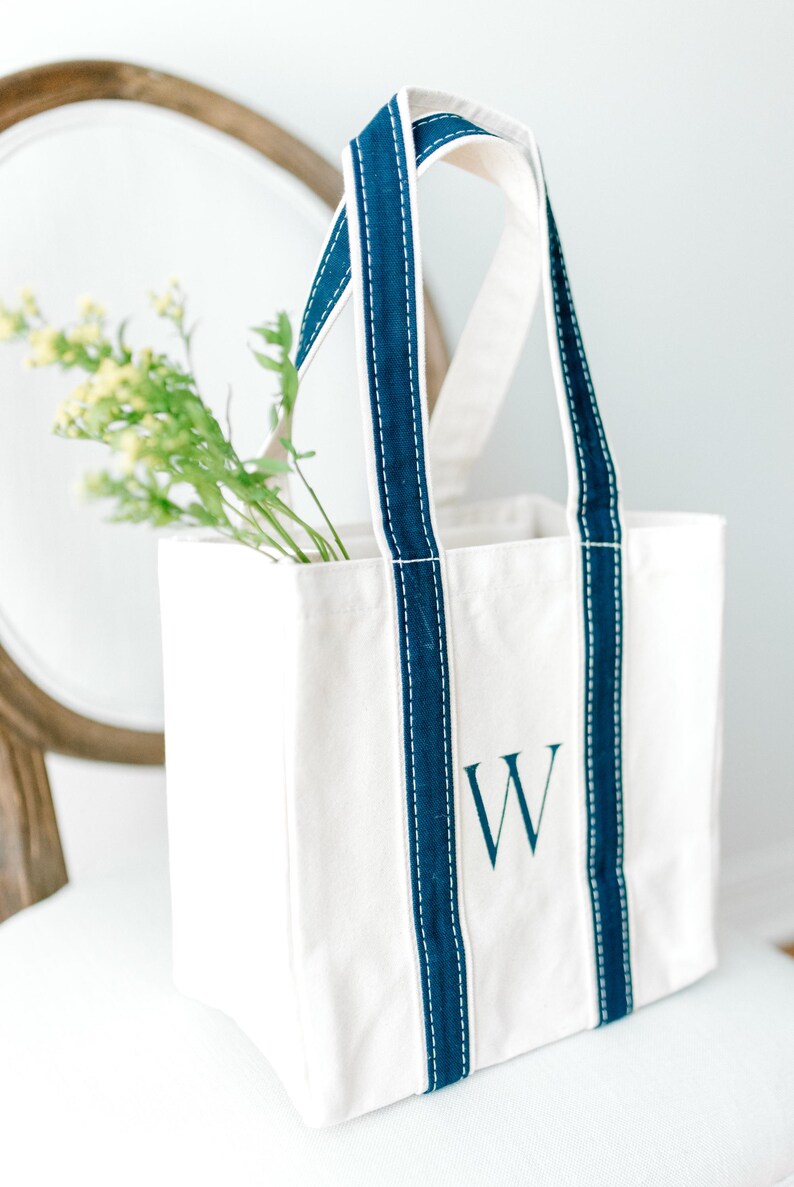 A natural canvas tote bag with navy blue straps and a navy blue hand painted letter "W" on the front.