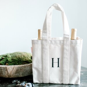 Natural canvas tote bag with two wine bottles inside and a black hand painted letter "H" on the front.