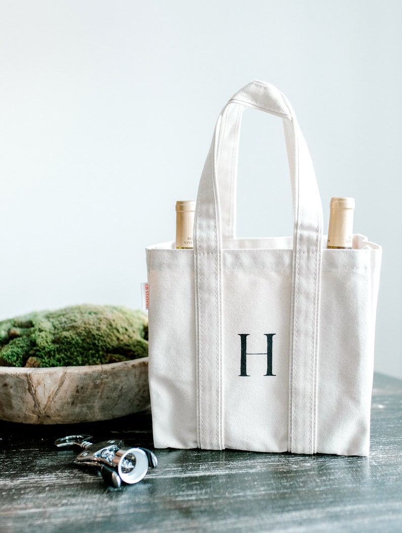 Natural canvas tote bag with two wine bottles inside and a black hand painted letter "H" on the front.