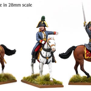 Op de afbeelding: Drie 28mm schaal miniatuurfiguren van militaire officieren te paard. De figuren dragen steekhoeden en lange jassen, gezeten op bruine en witte paarden. Elk staat op een rechthoekige basis met groen gras. Tekst: Models shown are in 28mm scale.