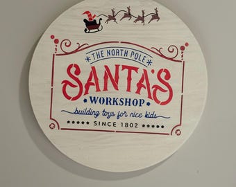 16 inch round Christmas door hanger.  Santa’s Workshop