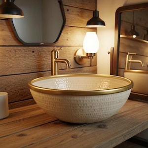Puede incluir: Un lavabo de cerámica texturizada de color crema con un borde dorado se encuentra sobre un mueble de baño de madera. Un grifo dorado está montado en el mueble. El fondo presenta una pared de madera, un espejo y accesorios de iluminación.
