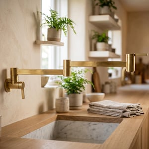 Op de afbeelding: Een aan de muur gemonteerde, scharnierende pannenvulkraan met een geborstelde messing afwerking. De armatuur heeft een lange, uitschuifbare arm met twee gewrichten en een enkele hendel aan de basis, gemonteerd op een getextureerde muur.
