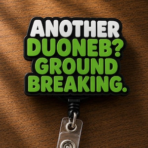 May include: A black badge reel featuring a rectangular topper with white text that reads ANOTHER and green text that reads DUONEB? GROUND BREAKING. The design has a thick black border and a clear plastic strap with a metal snap button at the bottom.
