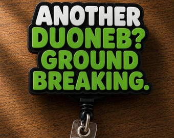 May include: A black badge reel featuring a rectangular topper with white text that reads ANOTHER and green text that reads DUONEB? GROUND BREAKING. The design has a thick black border and a clear plastic strap with a metal snap button at the bottom.