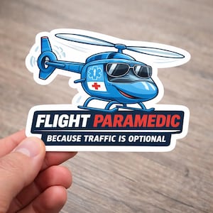 May include: A blue helicopter sticker with a smiling face and sunglasses. The sticker has the words "FLIGHT PARAMEDIC" in white and red text, with the tagline "BECAUSE TRAFFIC IS OPTIONAL" in white text.