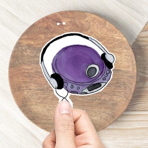 May include: A purple CD player with headphones attached. The CD player is on a wooden surface.