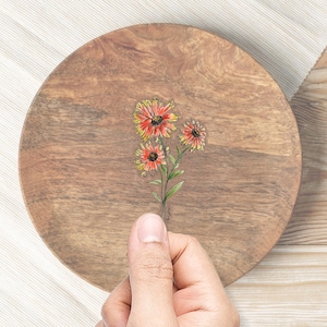 May include: A wooden plate with a hand-drawn illustration of a bouquet of orange and yellow flowers with green stems.