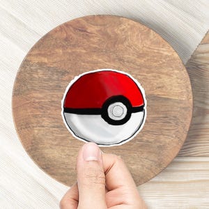 May include: A red and white Poke Ball sticker on a wooden surface.