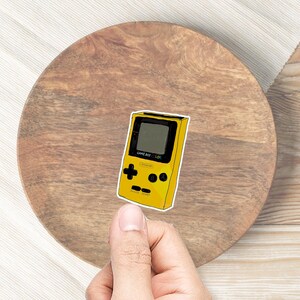 May include: A yellow Game Boy Color handheld video game console with a black screen and buttons. The console has the text "GAME BOY COLOR" printed on the front.