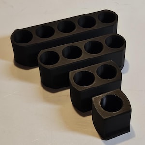 May include: Four black, rectangular holders with circular openings. The holders vary in size, with one holding five openings, another three, a third two, and the smallest one opening. The holders are arranged in a diagonal line.