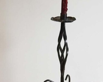 May include: A tall, wrought-iron candlestick with a twisted stem and a circular base. A red candle sits atop a decorative, scalloped holder. The candleholder is approximately 30 cm tall.