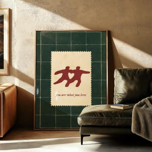May include: Framed art print featuring a dark green grid background with a postage stamp design. The stamp shows two figures with a heart shape between them, and the text "you are what you love".