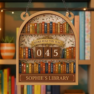 May include: Wooden bookshelf-shaped sign with the text "BOOKS READ THIS YEAR" and "SOPHIE'S LIBRARY". The sign has a decorative floral background and miniature book details. The number "045" is displayed on wooden blocks.