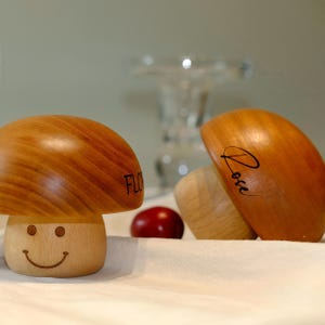 Peut inclure: Objets en forme de champignon en bois avec un fini grain de bois naturel. L'un a un visage souriant et le mot "FLO" sur le chapeau. Un autre a le mot "Rose" sur le chapeau. Une petite sphère rouge est également présente.