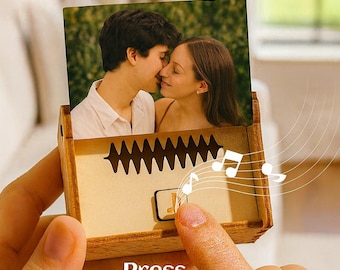 Puede incluir: Caja de música de madera con una fotografía de una pareja besándose. La caja tiene un diseño de onda de sonido y las palabras "Press Play Music" impresas en la parte inferior. Notas musicales ilustradas alrededor.