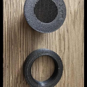 May include: Two black, textured, circular objects on a wood grain surface. The top object has a mesh centre and the text "30 mm". The bottom object is a ring with a textured surface.