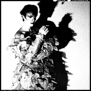 May include: Black and white album cover featuring a person in a textured outfit with the text "Scary Monsters" and "And Super Creeps". The image has a high-contrast, grainy texture, with a large shadow.