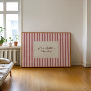 Pu&ograve; includere: Una grande stampa rettangolare incorniciata con un motivo a righe verticali rosa e bianche. Al centro, un pannello rettangolare color crema con bordo cucito contiene il testo corsivo marrone, your custom text here.