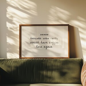 May include: A framed print with the text "barista was cute, would have coffee here again" in a handwritten style. The frame is brown, and the print is displayed above a green sofa.