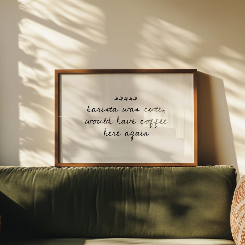 May include: A framed print with the text "barista was cute, would have coffee here again" in a handwritten style. The frame is brown, and the print is displayed above a green sofa.
