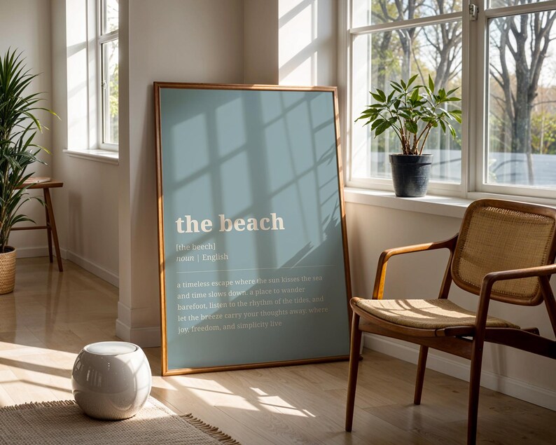 Puede incluir: Un p&oacute;ster enmarcado con las palabras "the beach" en una fuente clara sobre un fondo azul p&aacute;lido. La habitaci&oacute;n incluye una silla de madera, una peque&ntilde;a planta en maceta y un taburete de cer&aacute;mica blanco. La habitaci&oacute;n tiene grandes ventanas.