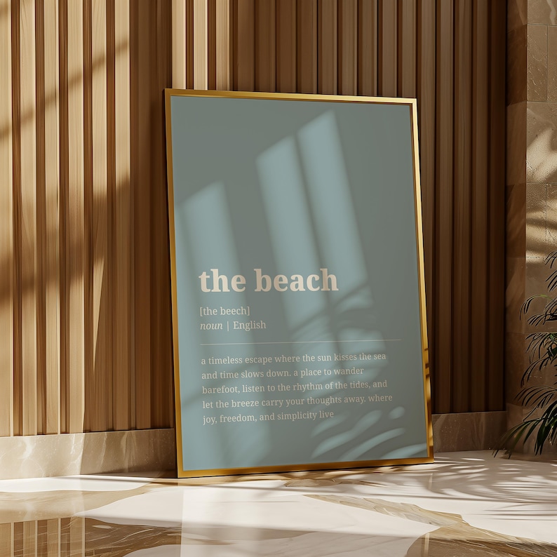 Puede incluir: Un marco dorado contra una pared de madera. El cartel muestra la palabra "the beach" en blanco sobre un fondo azul claro. El texto incluye una definici&oacute;n de la palabra, en ingl&eacute;s.