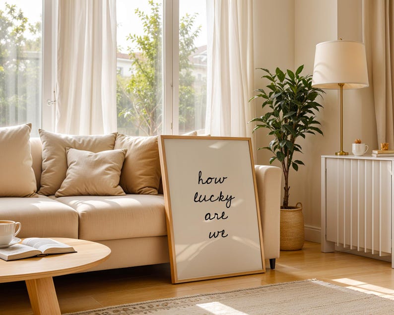 May include: A bright living room featuring a beige sofa with cushions, a wooden coffee table, and a framed print with the words "how lucky are we". A floor lamp, a potted plant, and a window with curtains create a warm, inviting atmosphere.