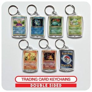 May include: Clear acrylic keyrings displaying double-sided Pokémon trading cards. Each keyring has a silver-coloured metal ring. The text "TRADING CARD KEYCHAINS" and "DOUBLE SIDED" is shown on a red banner.