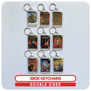 May include: A selection of double-sided Xbox keyrings showcasing game covers, including Halo and Star Wars Knights. Each keyring has a silver ring and a clear, rectangular design. The text "XBOX KEYCHAINS DOUBLE SIDED" is visible in a red and white banner.