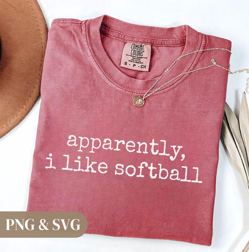 K&ouml;nnte beinhalten: Ein staubrosafarbenes T-Shirt mit dem wei&szlig;en Aufdruck "apparently, i like softball". Eine silberne Halskette mit einem kleinen Anh&auml;nger liegt auf dem Shirt. Das Shirt ist mit "Comfort Colors" gekennzeichnet und hat die Gr&ouml;&szlig;e S.