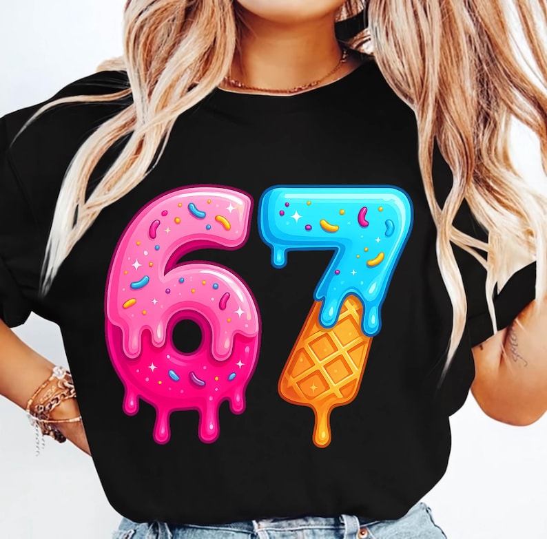May include: Black t-shirt featuring the number "67" in a playful, colorful design. The "6" is pink with sprinkles and a donut shape, while the "7" is blue with a waffle cone base. A fun, celebratory graphic.