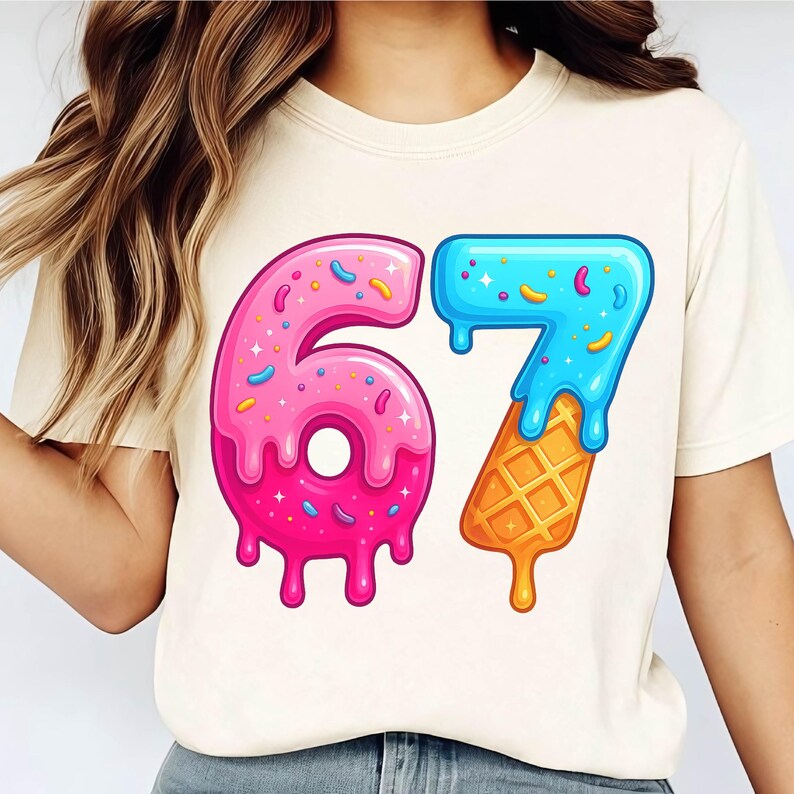 May include: Cream-colored t-shirt featuring a colorful graphic of the number "67". The "6" is pink with sprinkles and the "7" is blue with a waffle cone base. The design has a dripping effect.