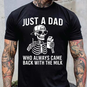 May include: Black t-shirt with a white graphic of a skeleton wearing sunglasses and a cap, holding a milk carton. The text reads "JUST A DAD WHO ALWAYS CAME BACK WITH THE MILK."