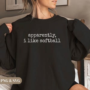 K&ouml;nnte beinhalten: Schwarzes Sweatshirt mit dem wei&szlig;en Text "apparently, i like softball". Das Sweatshirt hat einen Rundhalsausschnitt und scheint aus einem weichen Material zu sein. Das Bild ist eine Nahaufnahme des Oberk&ouml;rpers.