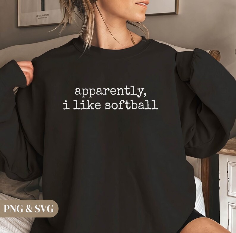 K&ouml;nnte beinhalten: Schwarzes Sweatshirt mit dem wei&szlig;en Text "apparently, i like softball". Das Sweatshirt hat einen Rundhalsausschnitt und scheint aus einem weichen Material zu sein. Das Bild ist eine Nahaufnahme des Oberk&ouml;rpers.