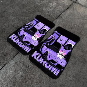 Könnte beinhalten: Ein Paar rechteckige schwarze Auto-Fußmatten mit einem violetten Grafikdruck eines Sportwagens und der Figur Kuromi. Der Text KUROMI ist in großen violetten Buchstaben am unteren Rand jeder Matte aufgedruckt, mit einem violett-schwarzen Farbschema.